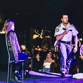 Male stripper dressed as a police officer performing for a seated guest on stage while a large crowd watches the live show.