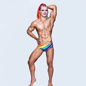 Rainbow Muscle Glam Brisbane drag performer striking a bold studio pose in rainbow briefs with red hair, dramatic makeup and a muscular physique.