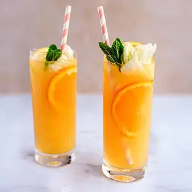 Two vibrant scorpion punch cocktails served in tall glasses with orange slices, mint leaves, whipped foam and striped paper straws on a marble surface, styled for tropical party drinks, cocktail recipe blogs and fun cocktail making classes.