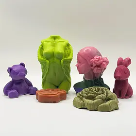 A collection of colourful, handmade artisanal soaps in various shapes, including a purple bear, a lime green feminine torso, a pink floral bust, a magenta rabbit, a green rose, and a brown paw print, made at LuckyLadds soap making class.