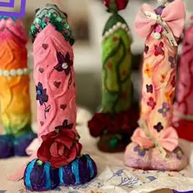A row of creative plaster and paint masterpieces from a "Design-a-Willy" workshop, featuring purple and orange phallic sculptures decorated with pink bows, lace, and floral patterns. These naughty risqué moulds are the ultimate hens party activity or birthday entertainment available Australia-wide.