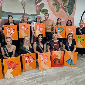 Paint and Sip Hens Party Hens party guests posing with their completed paint and sip artworks alongside a professional topless waiter during a creative hens party activity.