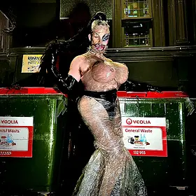 Queensland drag queen Asphyxia posing beside commercial bins in an avant-garde fashion outfit made from clear plastic wrapping.