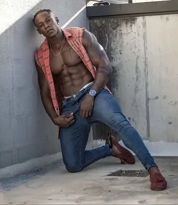 O’Niel posing shirtless in an open red check shirt and fitted jeans, available to book as a Sunshine Coast topless waiter.