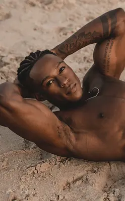 O’Niel reclining shirtless on the sand with his arms behind his head, available to book for Sunshine Coast party entertainment.
