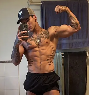 Ben taking a shirtless mirror selfie while flexing his tattooed arm, available to book for Sunshine Coast hens nights and private parties.