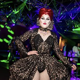 Delvira Nightclub Royalty Perth drag queen Delvira posing in a dramatic black and gold gown under colourful nightclub lighting, available to hire for parties and events.
