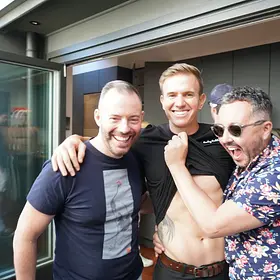 LuckyLadds waiter laughing with two male guests as they cheekily lift his black shirt during a fun private party.