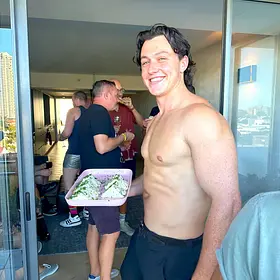 Sam Party Smile Sam smiling shirtless in black pants while mingling with guests at a private party, available to hire as a Sydney topless waiter for hens parties and events.